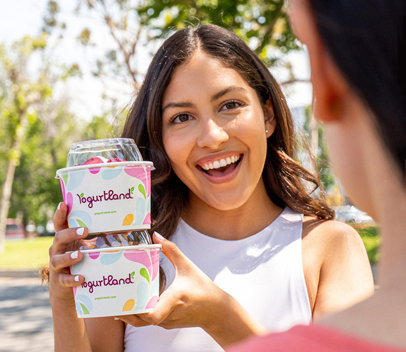 A woman holding up a cup of Yogurtland frozen yogurt.