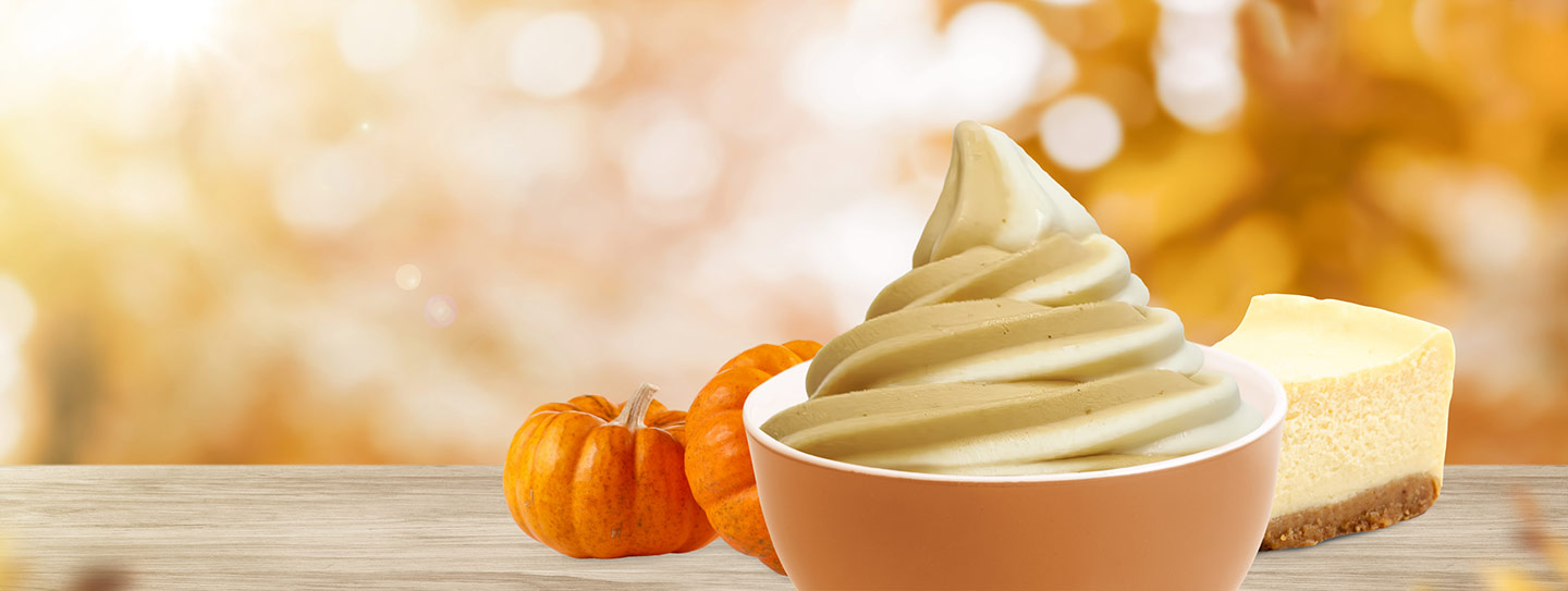 A cup of frozen yogurt alongside pumpkins and a slice of cheesecake